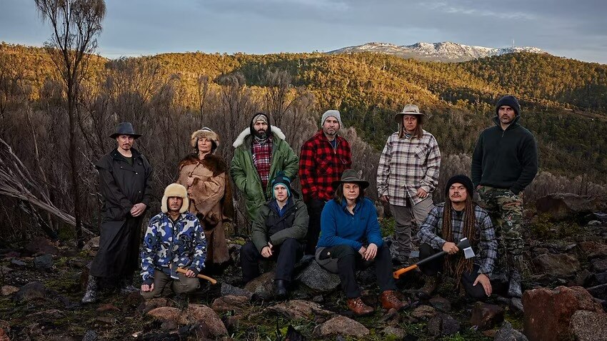A group in winter clothes stands in a remote location with snowcapped mountains in the distance