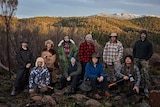 A group in winter clothes stands in a remote location with snowcapped mountains in the distance