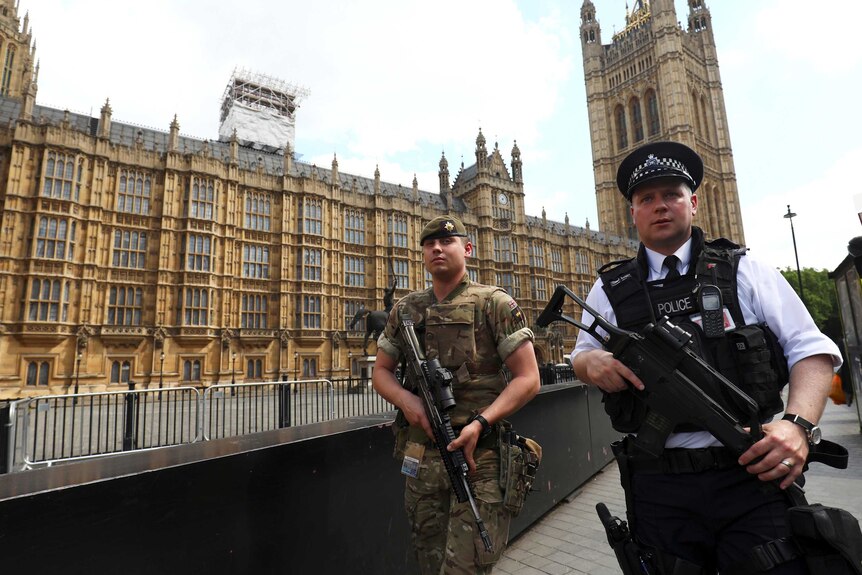 A soldier and police officer walk past UK's Houses of Parliament.