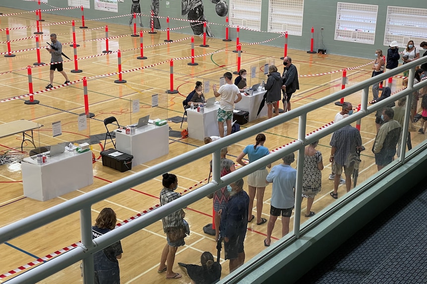 People stand in line to be tested at a gymnasium.