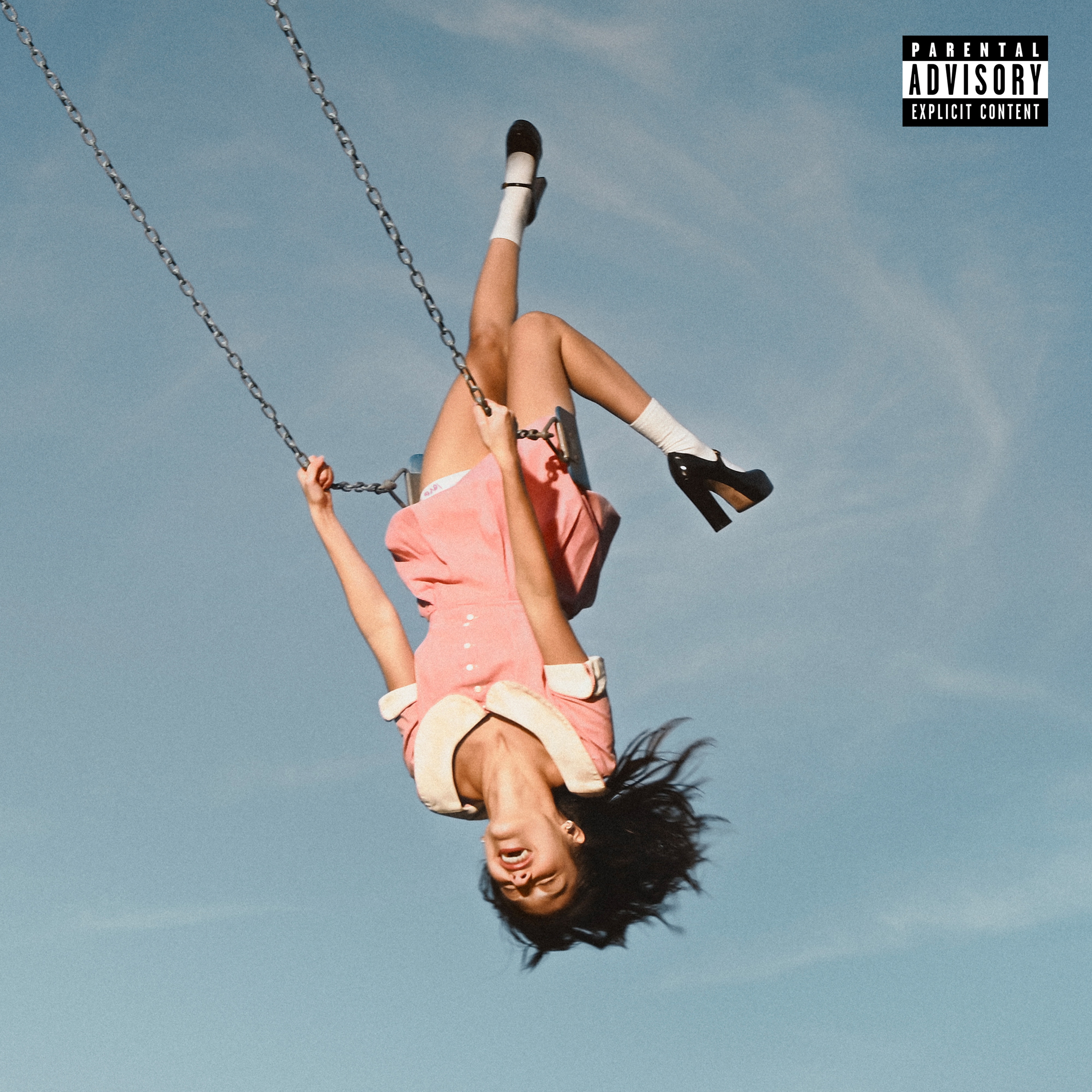 a girl in a pink and white school girl dress hanging upside down on a swing with only blue sky behind her