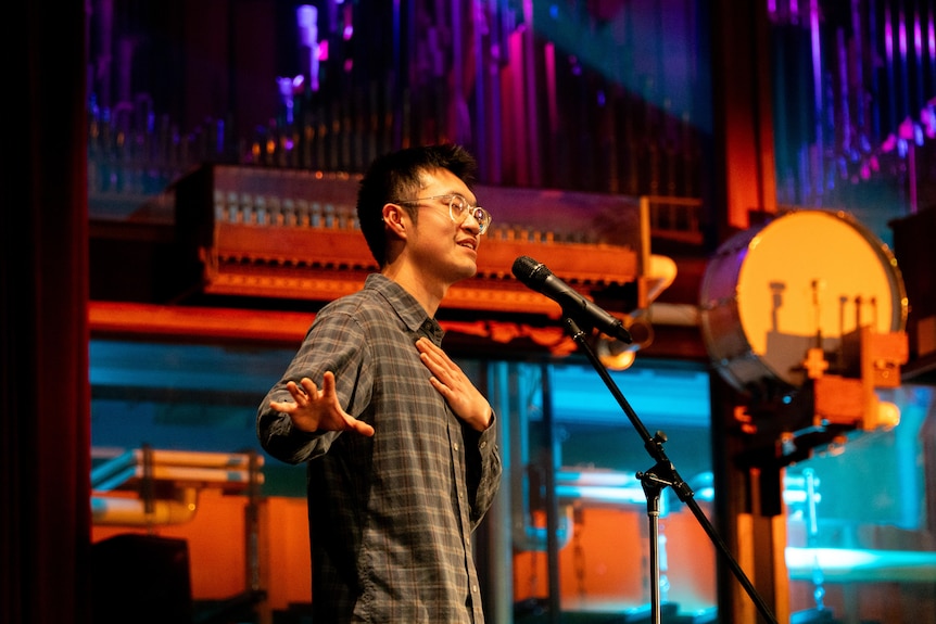 A man stands up in front of a microphone on stage.