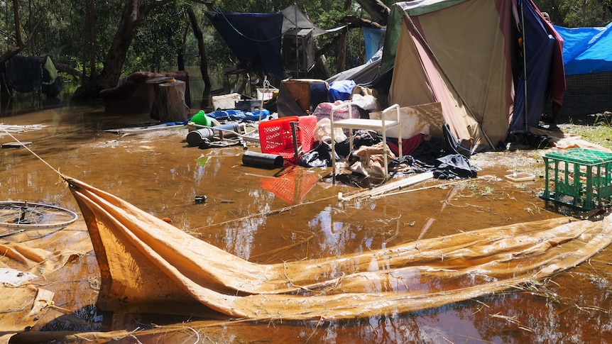 Shelving, shade sails, multiple tents and personal items lie in a pool of floodwater.