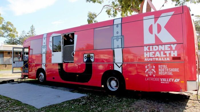 Big red bus purpose built for people to receive dialysis parked with a woman waving from inside