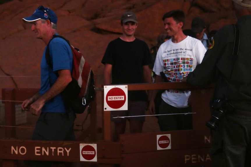 Three white men of varying ages smile as they walk away from Uluru.