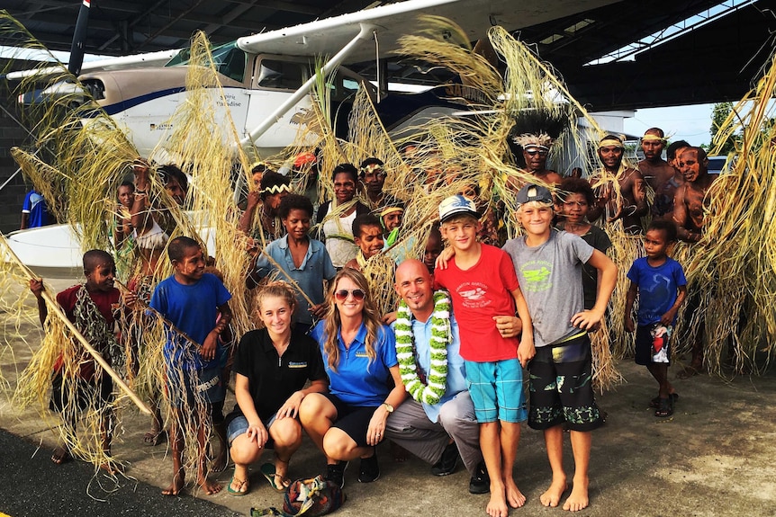 Mark Palm and his family are surrounded by traditionally-dressed locals in front of a float plane