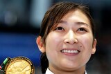 A smiling woman holds up her gold medal.