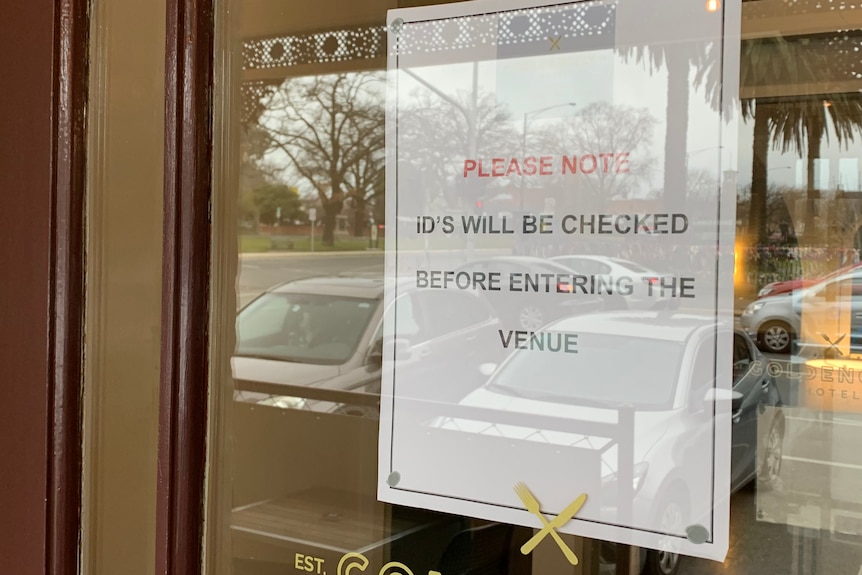 An A4 sign on a glass pub window saying "IDs will be checked" on entry.