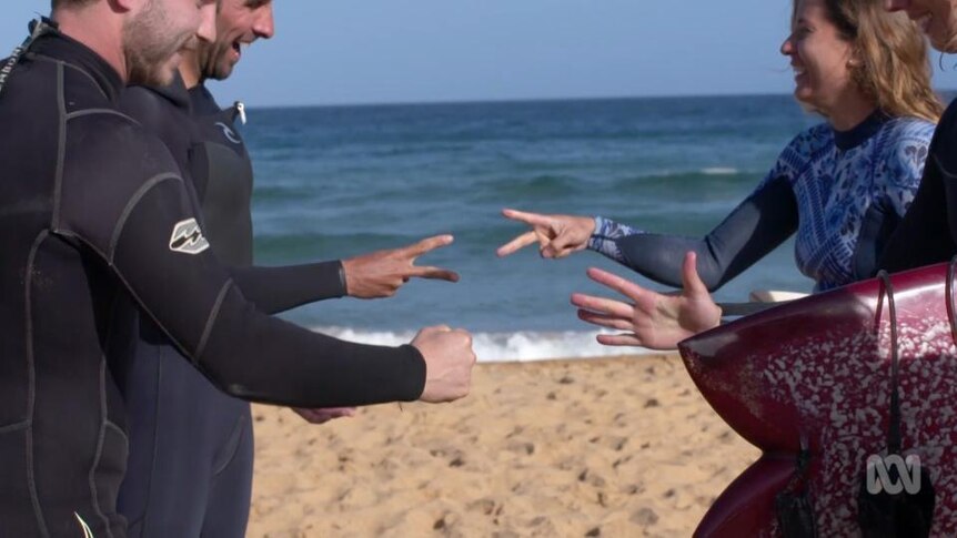 Men and women play rock paper scissors with their hands at the beach