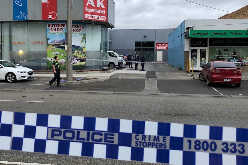 A parking area between a supermarket and a massage parlour is cordoned off with police tape.