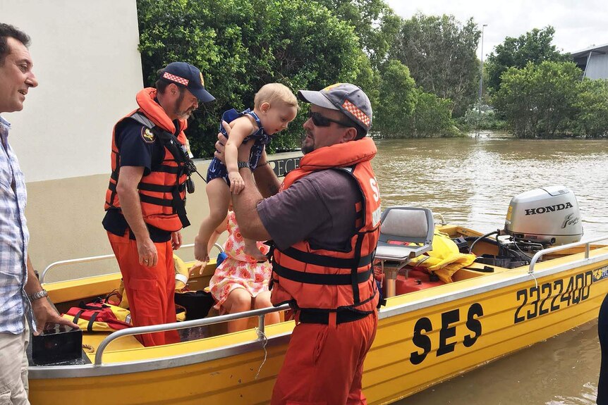 Two SES volunteers help a man and a baby into a boat in the flooded town of Ingham