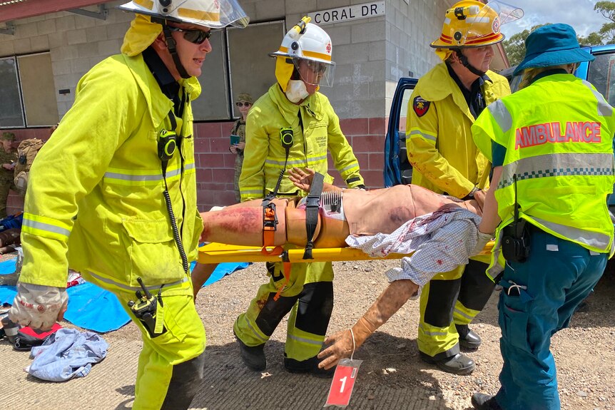 Four emergency service personnel carry a stretcher with a training dummy on it.