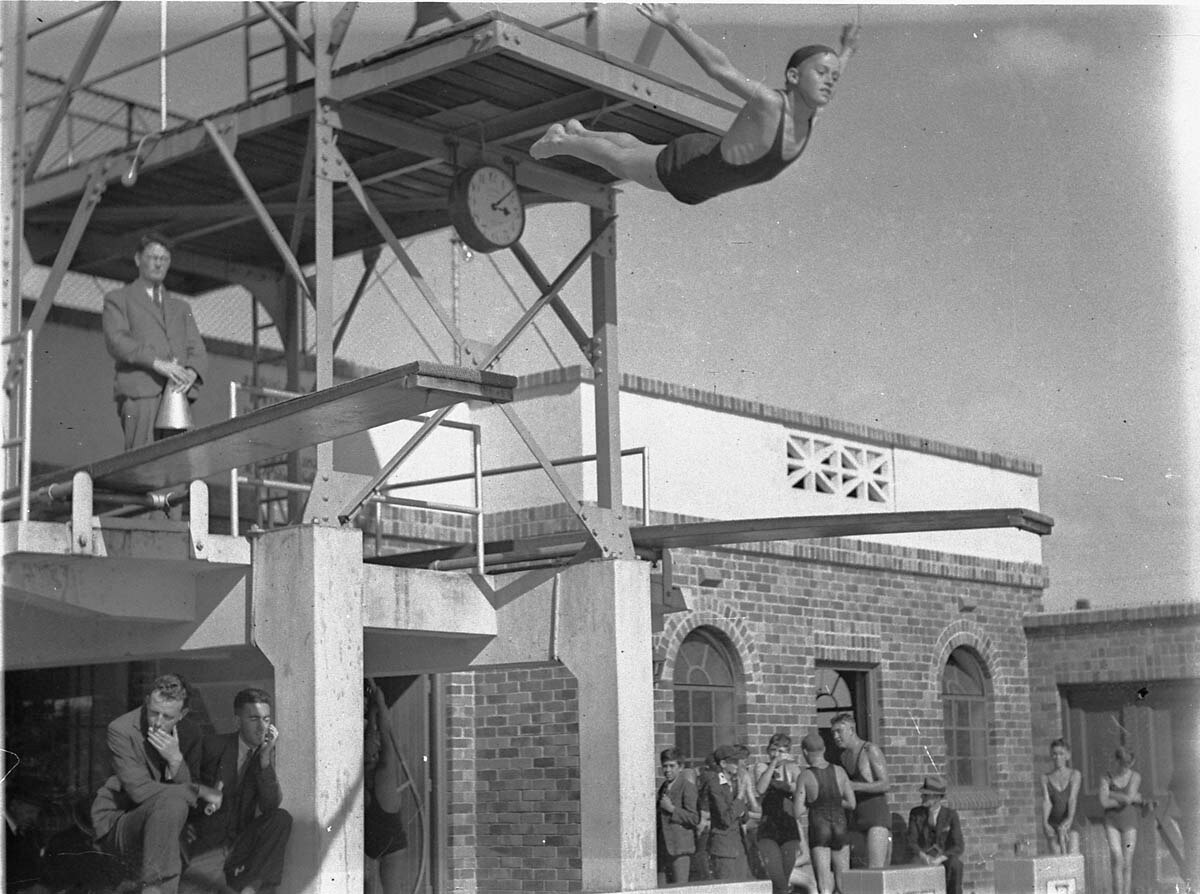 A black and white photo of a boy mid air with the diving board behind him