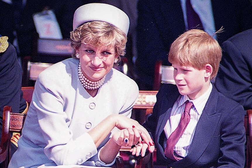 Princess Diana in a purple suit sits smiling next to a young Prince Harry dressed in a suit and tie