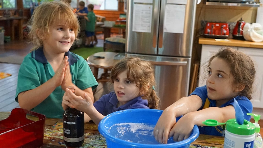 Three children wash their hands in a tub of water.