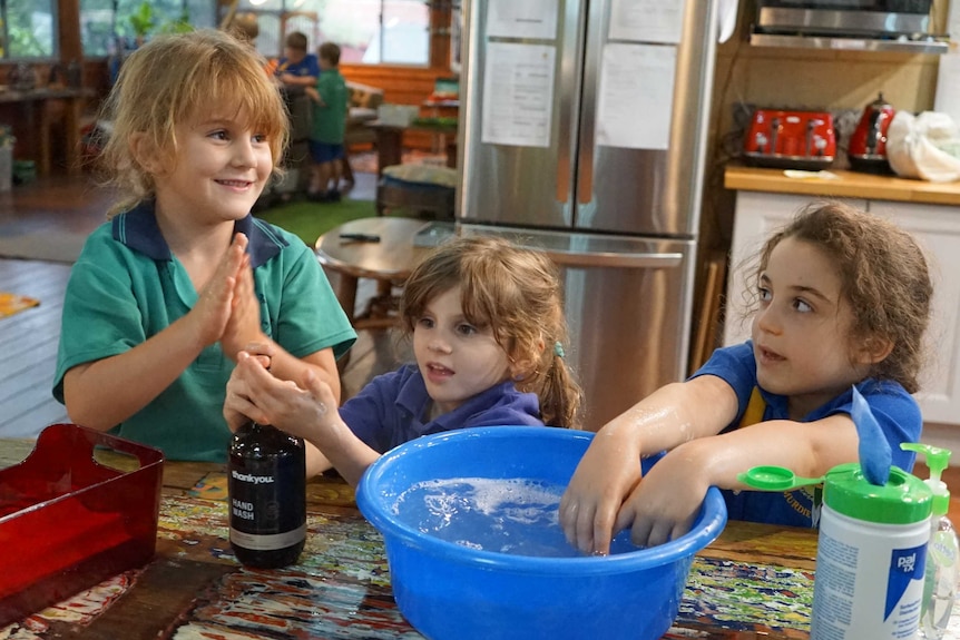 Three children wash their hands in a tub of water.