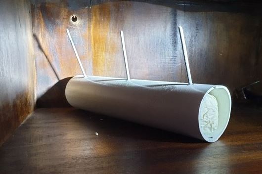 A close-up shot of a homemade white pipe bomb, with three sticks protruding from the top, on a wooden shelf.