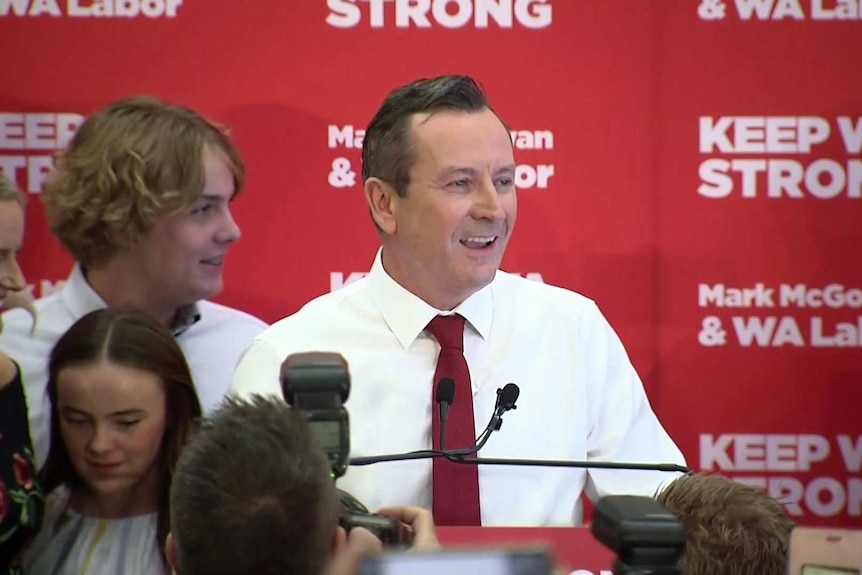 Mr McGowan smiles at the podium, his wife and children behind him.