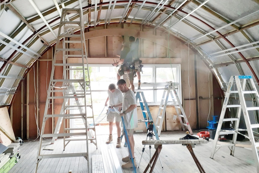 Builders working inside a Nissen Hut, which has been stripped back to it's structure and roof.