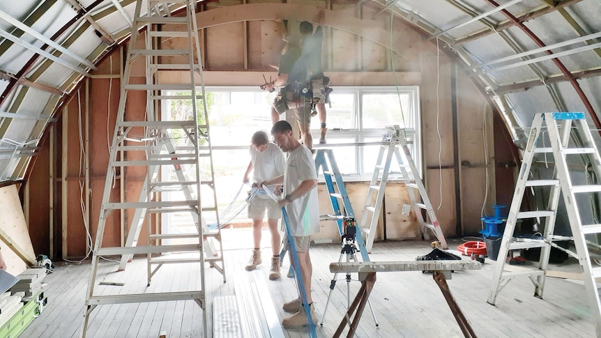 Builders working inside a Nissen Hut, which has been stripped back to it's structure and roof.