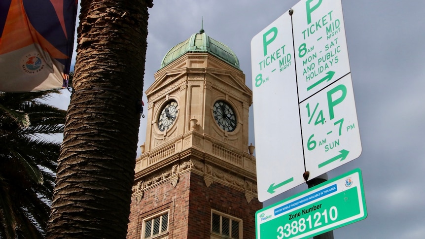 A ticketed car parking sign in front of a clock tower and grey sky.