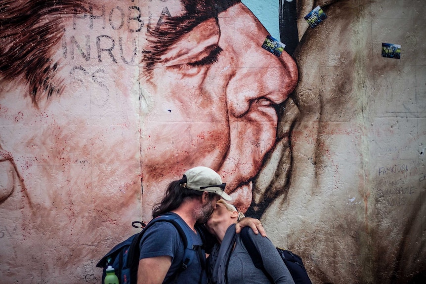 Kathrin and her husband in front of the famous mural painting of the kiss, imitating the kiss