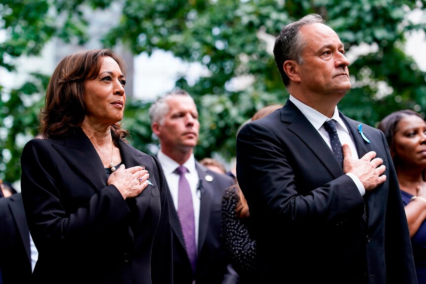 VP Kamala Harris puts right hand to heart standing next to her husband at solemn outdoor ceremony