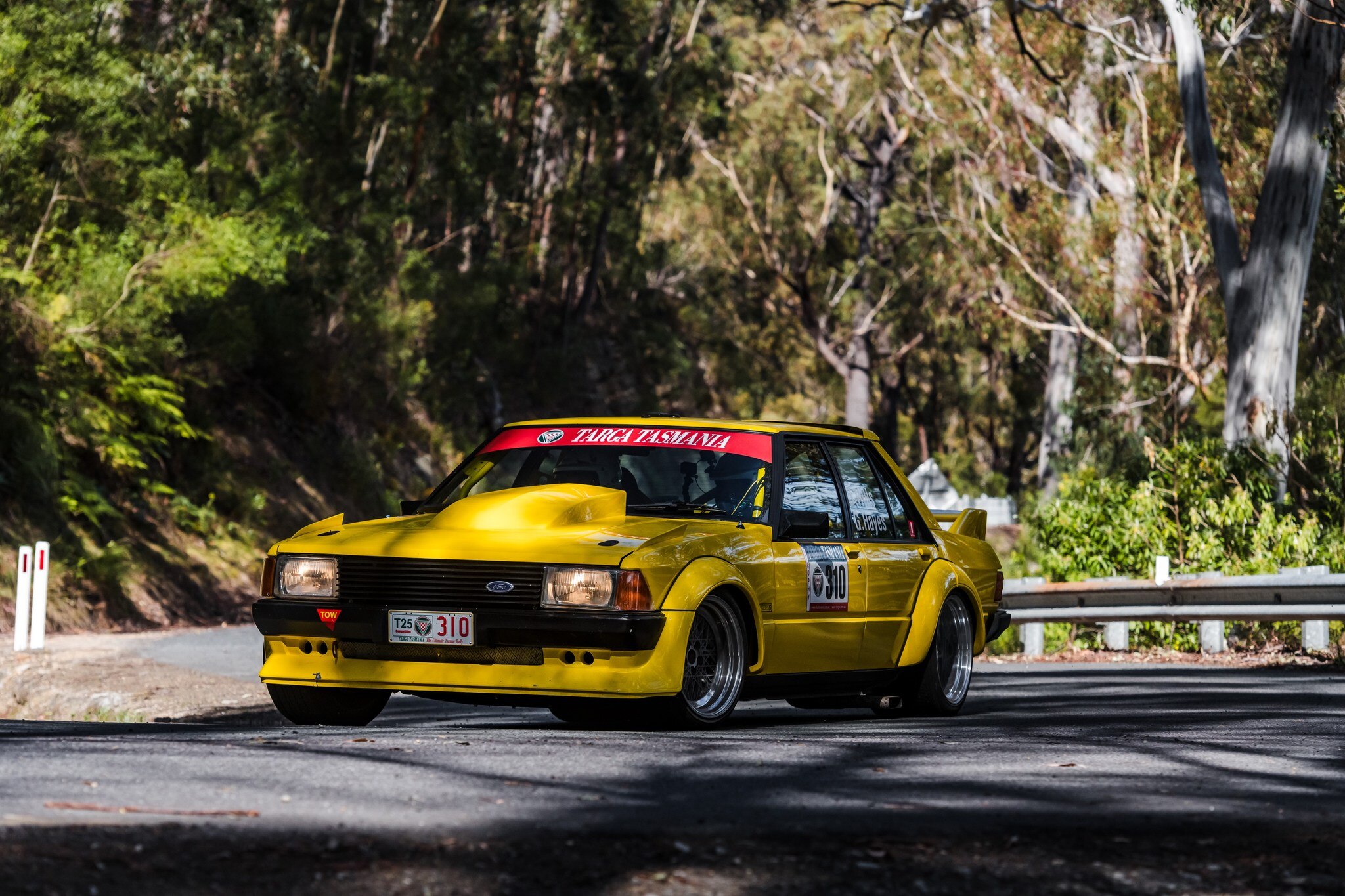 A yellow car on a winding road flanked with trees.