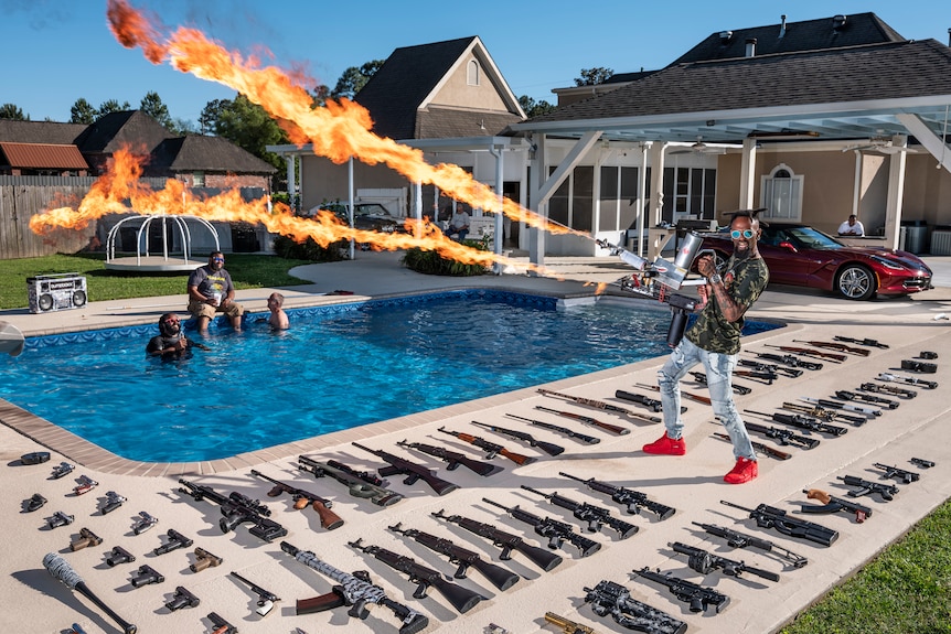 Un homme pose avec ses armes à feu et son lance-flammes dans l'arrière-cour de sa maison.