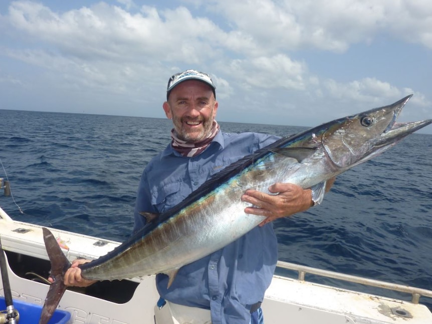 A smiling man on a boat holding a large wahoo fish.