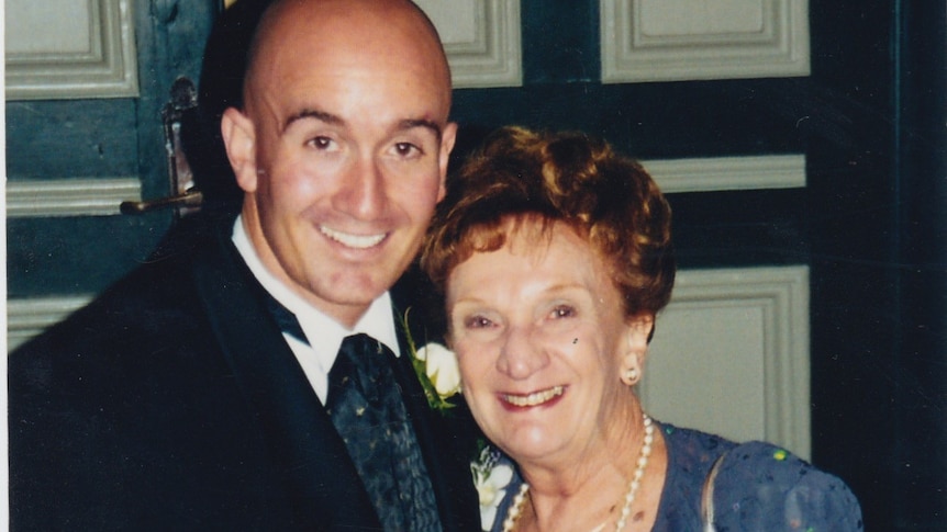 Simon Kennedy, dressed in formal suit, with his arm around his mother, Yvonne, in formal purple dress. Both are smiling widely.