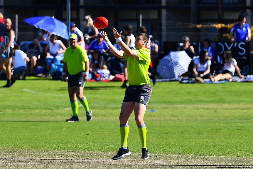 An Australian rules football umpire throws the ball into the air. 