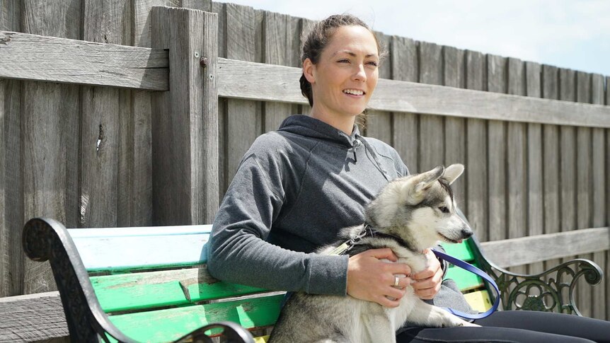 AFLW player Meg Downie sits on a bench with her dog.