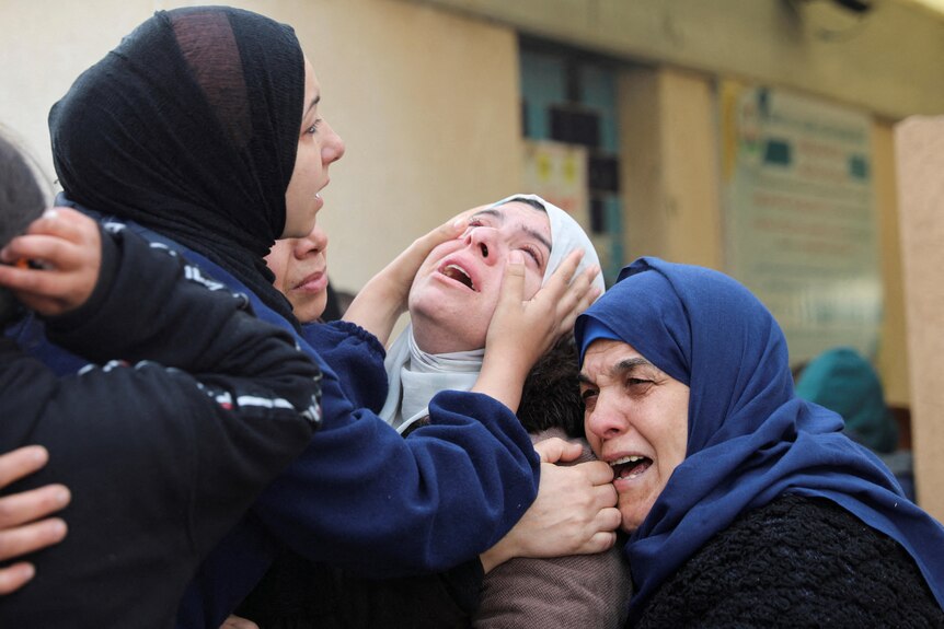 Three women cry and embrace at a funeral.