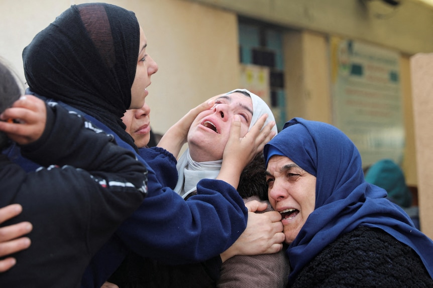 Three women cry and embrace at a funeral.