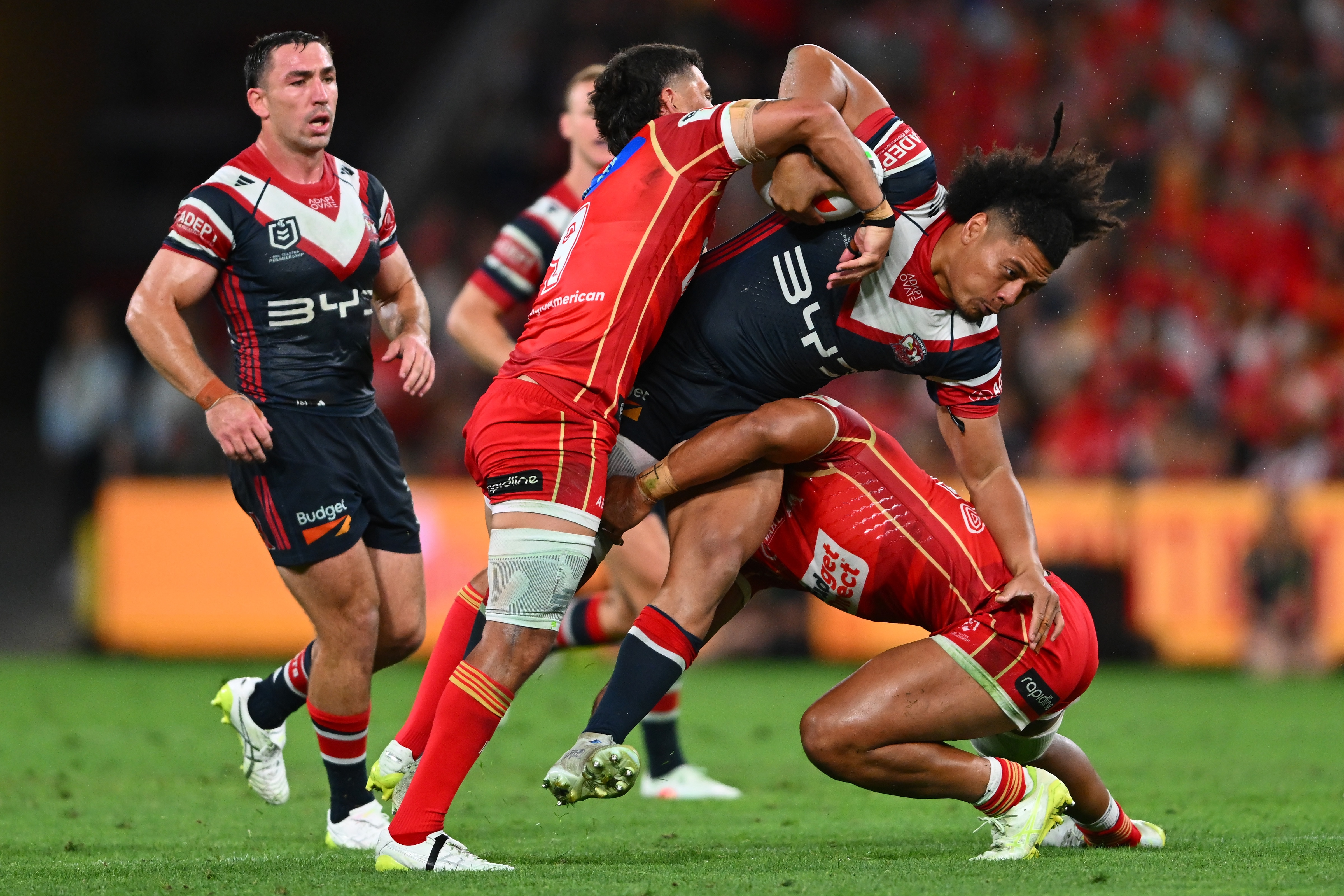 Naufahu Whyte of the Roosters is tackled by two Dolphins players
