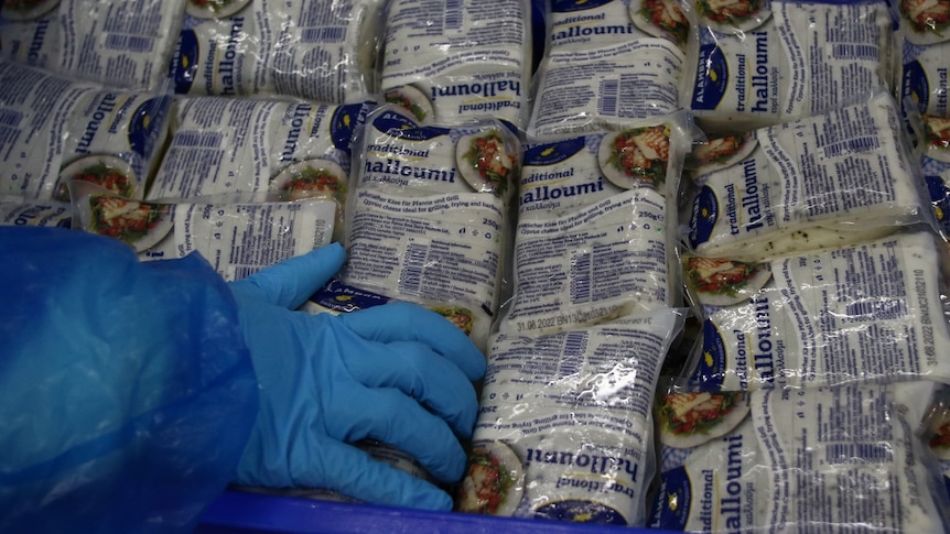 hands in blue gloves grab packets of halloumi stacked inside a blue crate