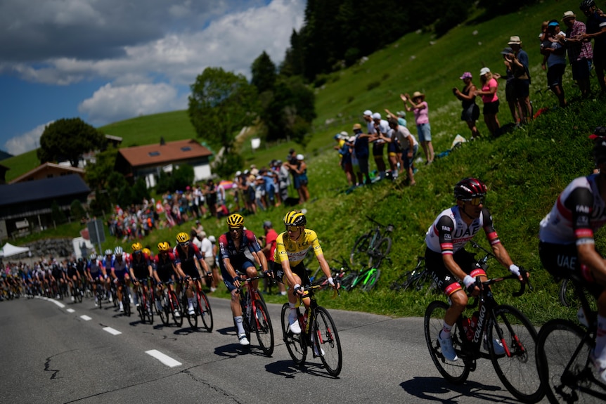 A cyclist in a yellow jersey rides comfortably at the Tour de France, with a line of his teammates riding behind him. 