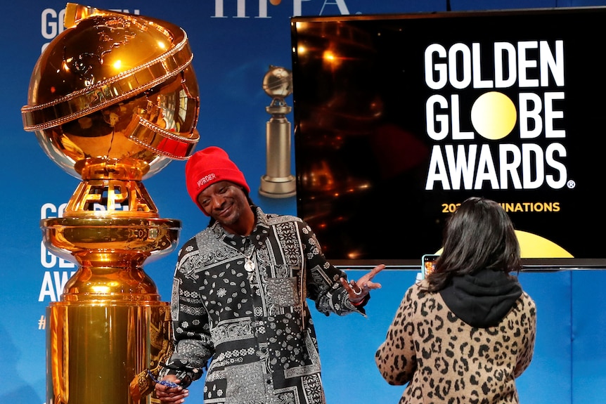 Snoop Dogg with his arms outstretched and a photographer in front of him, a large golden globe behind him