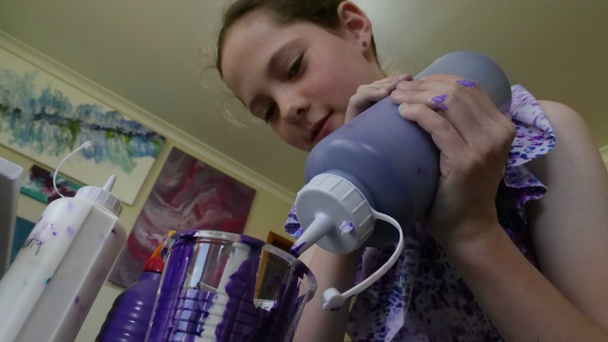 Young girl squeezing a large bottle of purple paint into a cup as she leans over it
