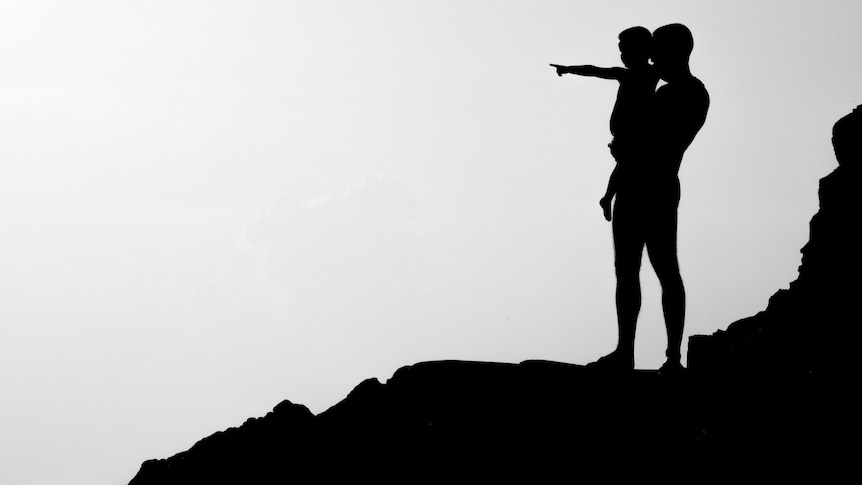 A parent and child's silhouette standing on top of rocks at the beach. 