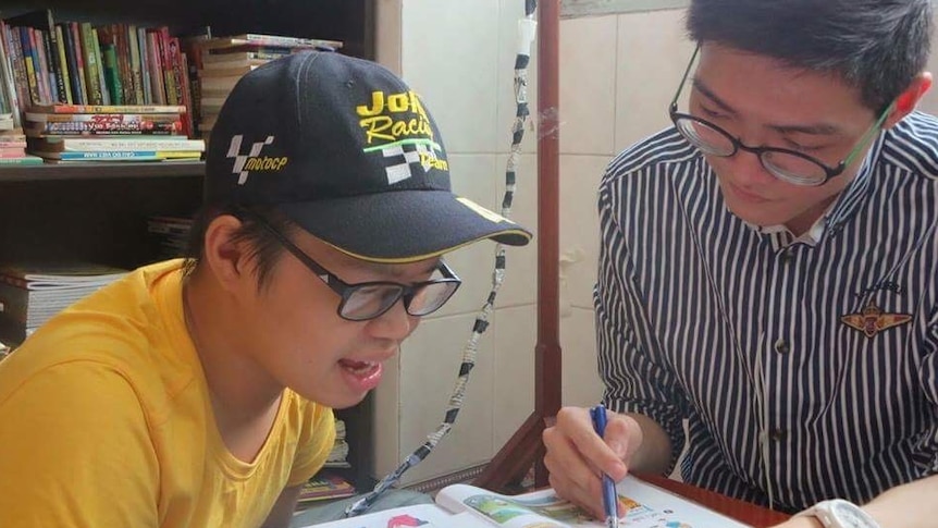 A teenager (left) reads from a textbook as a young man (right) points to a section of the page.