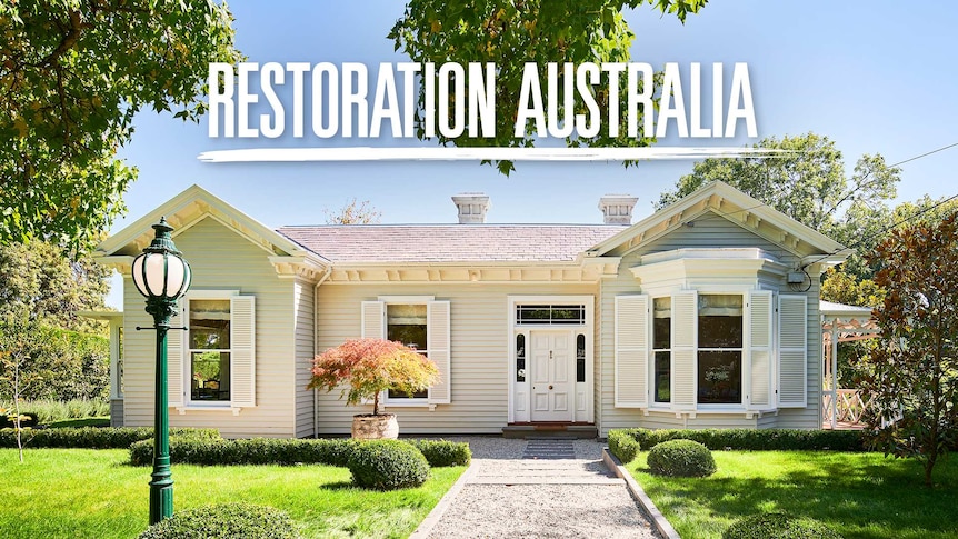 White single story heritage home with ornate lamppost at the front, surrounded by trees and blue sky