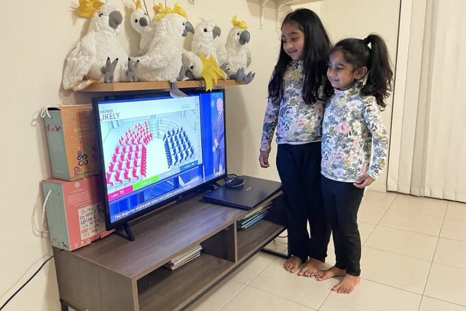 Two little girls watch election results on a TV.