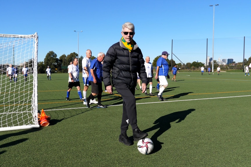 a man in a puffer jacket and sunglasses with a football at his feet
