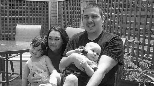 Black and white photograph of Tom Roberts seated in a chair with his wife Teja and two children.