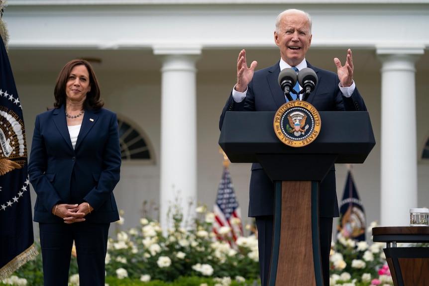 US Vice President Kamala Harris listens as President Joe Biden speaks at a podium in the Rose Garden of the White House