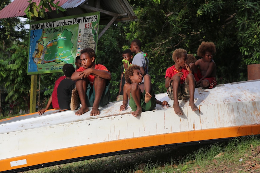 A few children sit on an upturned boat.
