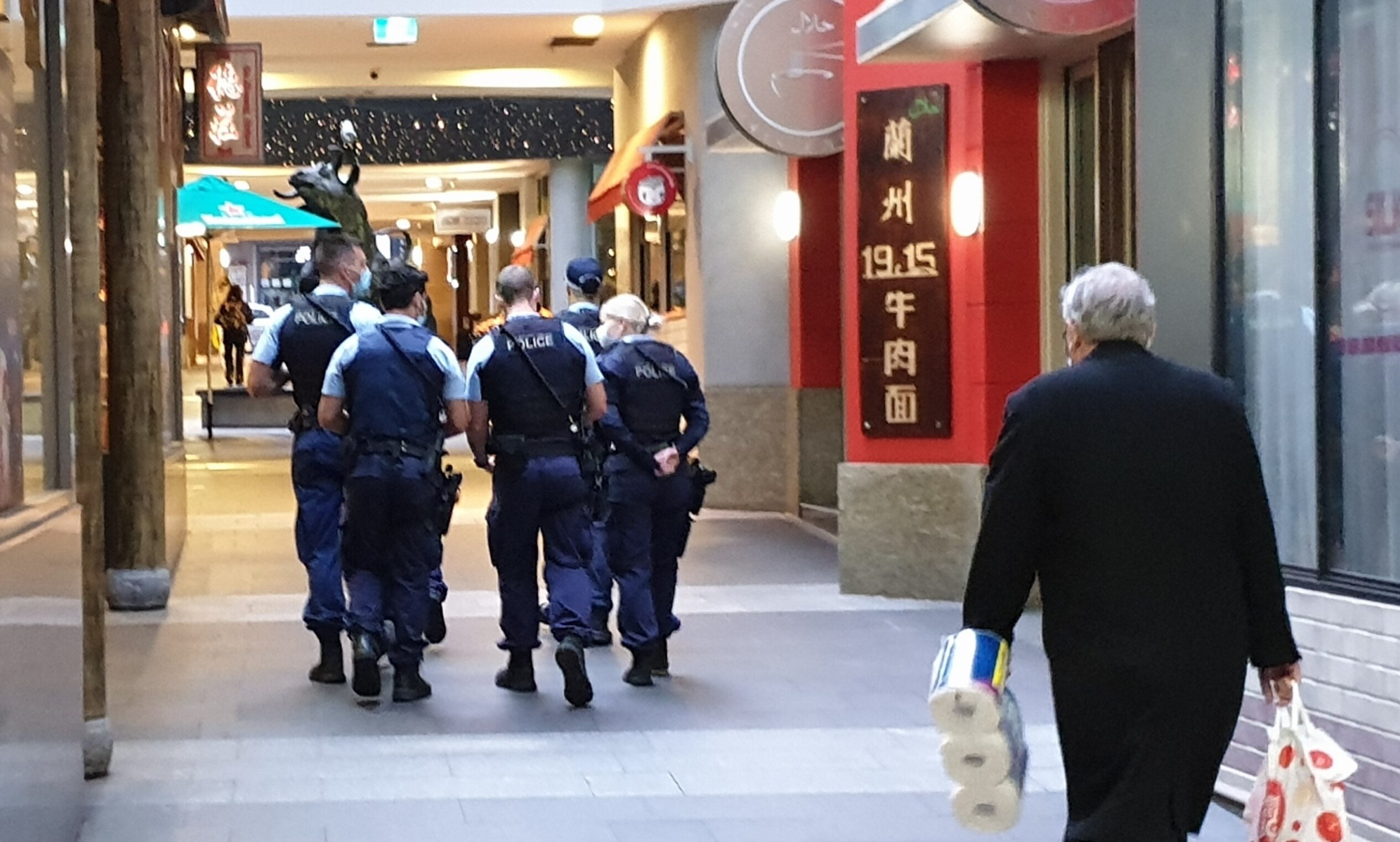 Five police officers patrolling World Square in the Sydney CBD, while an old man walks behind them.