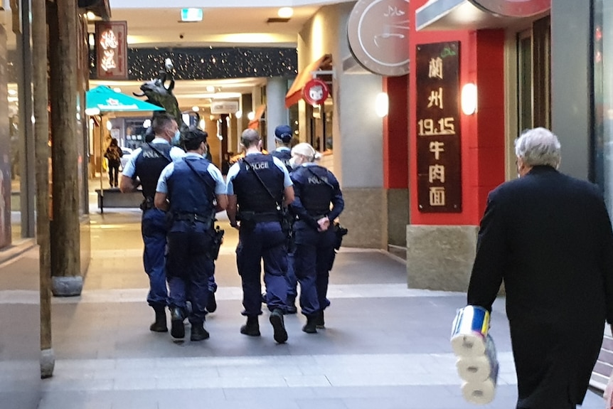 Five police officers patrolling World Square in the Sydney CBD, while an old man walks behind them.
